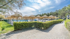 Ein Poolbereich mit Reetsonnenmarkisen, einem gepflasterten Weg und ordentlich geschnittenen Hecken.