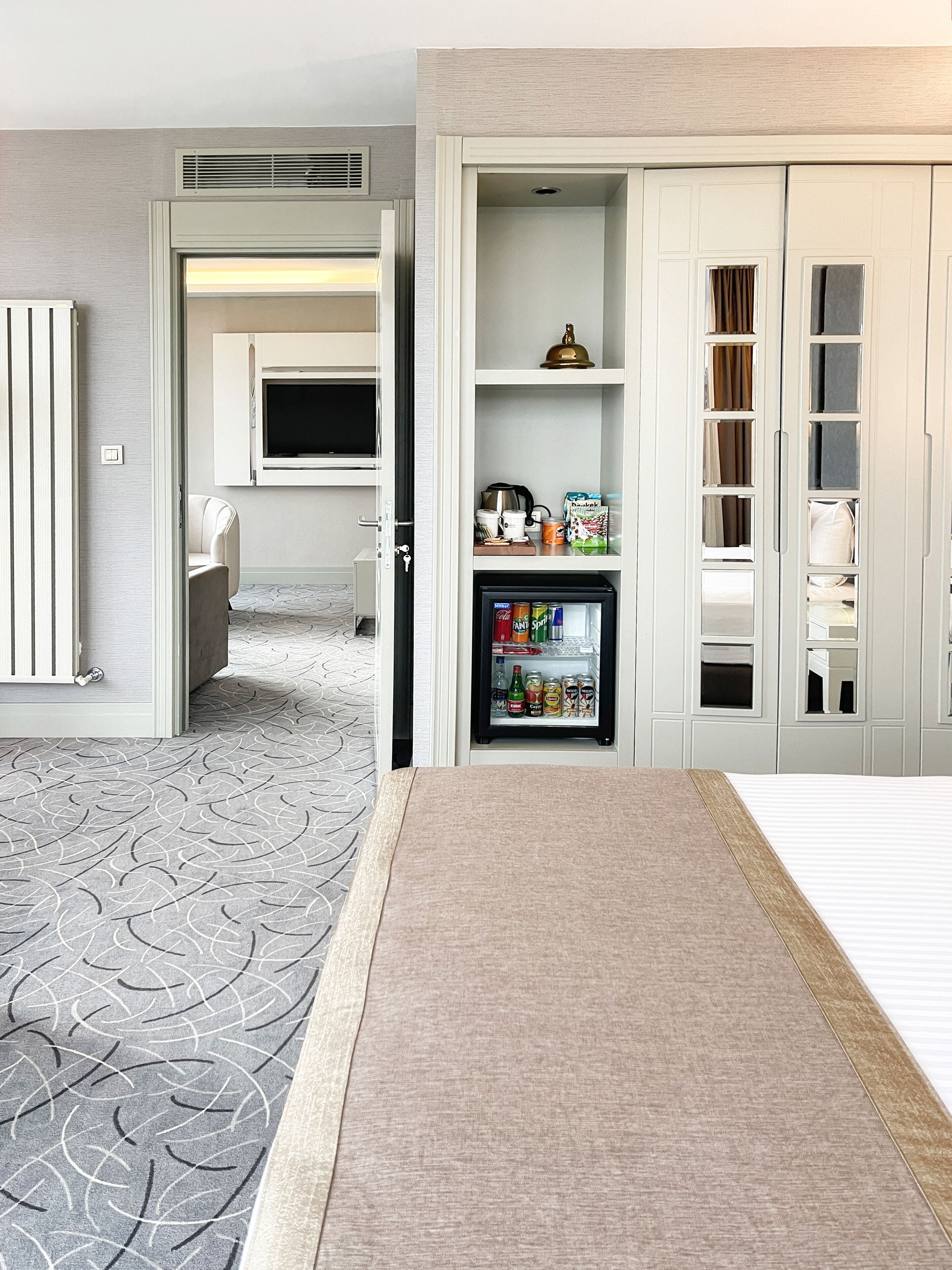 A hotel room with a minibar, a television, a bed, and a patterned carpet.