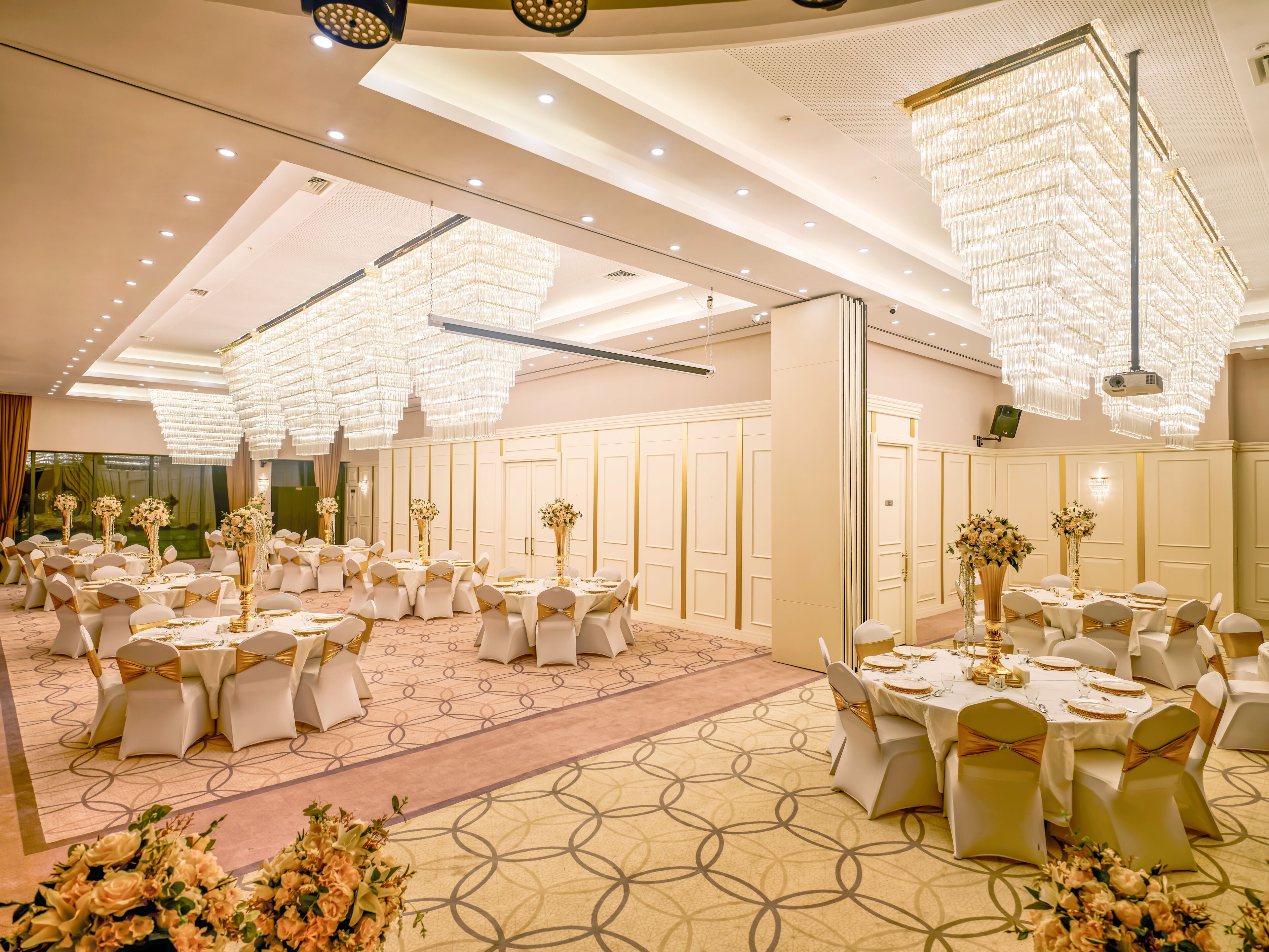 A banquet hall with round tables, white chairs, and chandeliers.