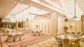 A banquet hall with round tables, white chairs, and chandeliers.