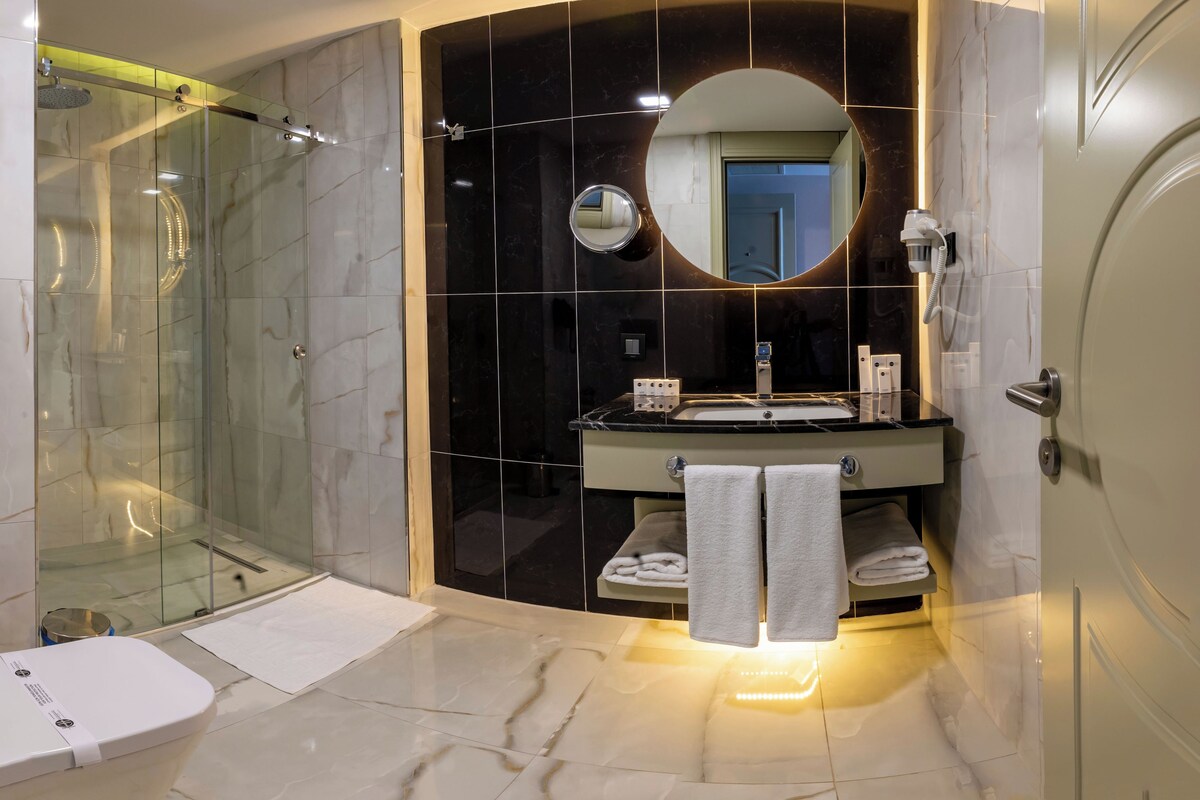 Une salle de bain moderne avec une douche à parois de verre, un meuble-lavabo doté d’un miroir rond et des toilettes.