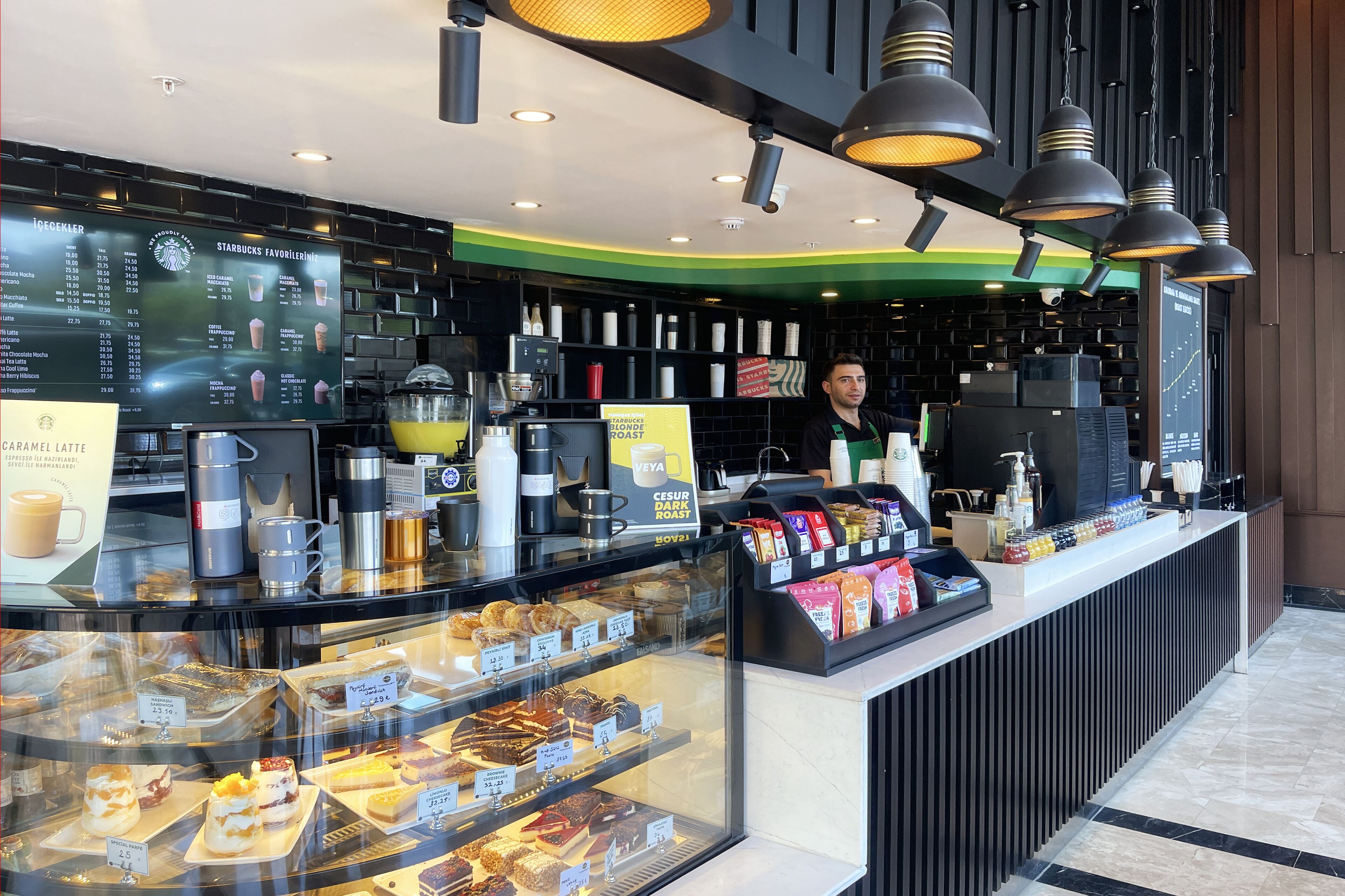 A Starbucks coffee shop with a menu board, a counter with pastries, and a coffee machine.