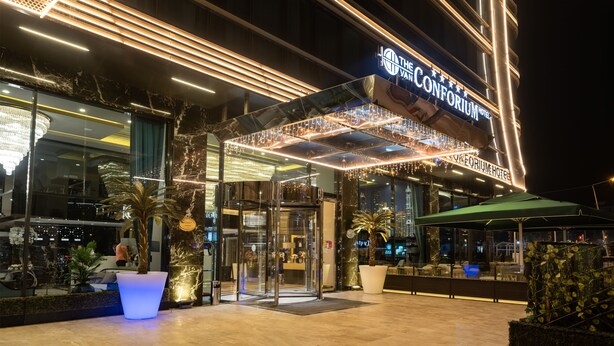The Conforium Hotel entrance with illuminated signage, a glass entrance, and outdoor seating area. - The Conforium Hotel Van (Van)