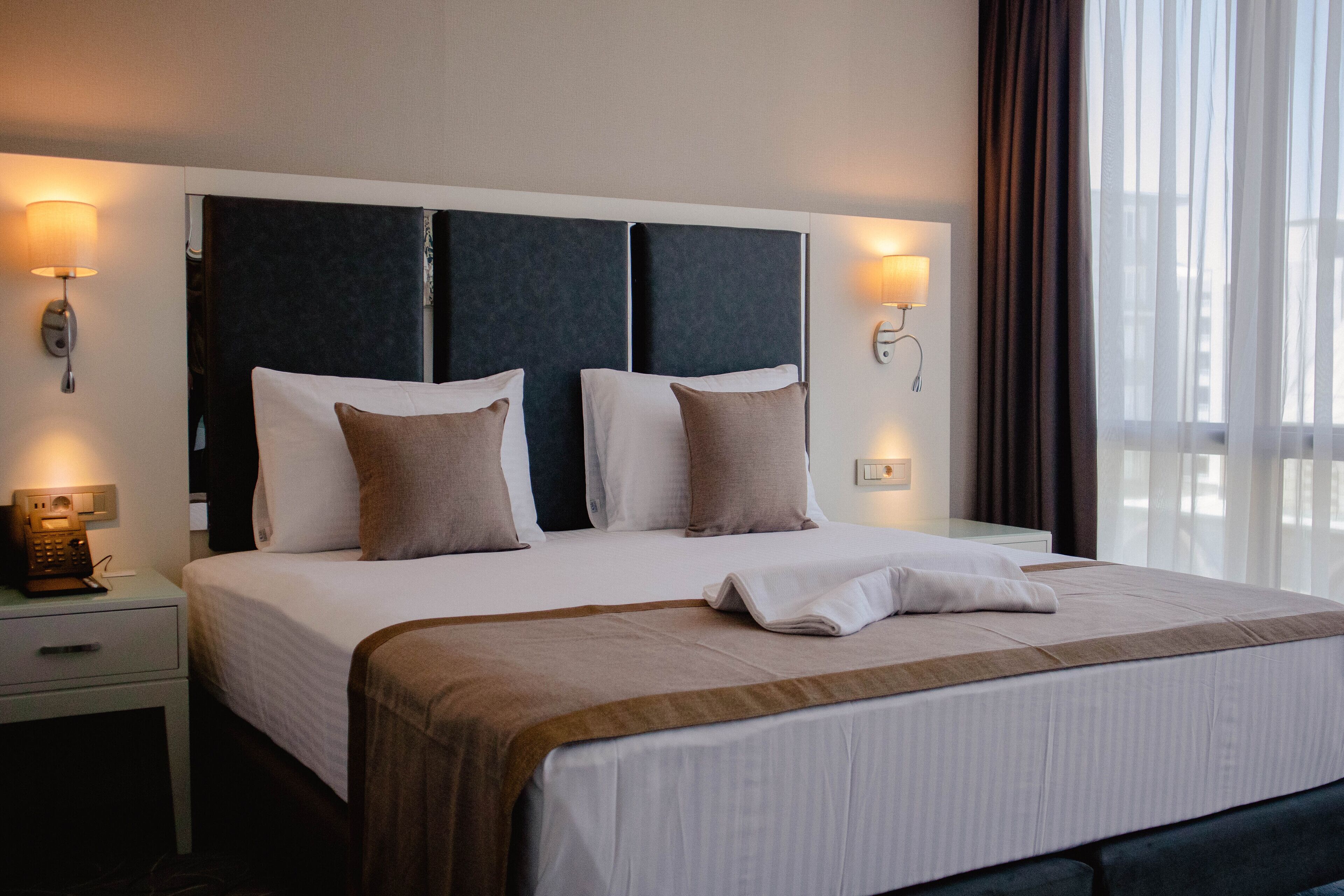 Una habitación de hotel con una cama grande, dos mesitas de noche y una lámpara.