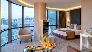A modern hotel room with a large bed, a sofa, a TV, and a dining table with fruit. - The Conforium Hotel Van (Van)
