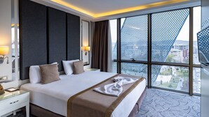 A hotel room with a large bed, a nightstand, a lamp, and a window with a view of the city. - The Conforium Hotel Van (Van)