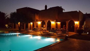 Un espace aménagé au bord de la piscine, avec des chaises longues et une piscine, au crépuscule.