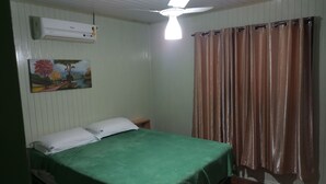 Ein Zimmer mit Bett, Deckenventilator, Klimaanlage, einem Bild und Vorhängen.