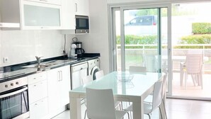 A modern kitchen with white cabinets, a glass dining table, and a view of the outdoors through a sliding glass door. - Modern, air-conditioned family apartment with pool. 10 minute walk to beach (Salir do Porto)