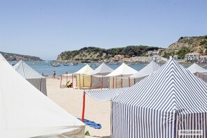 A beach with striped tents and a view of boats on the water. - Modern, air-conditioned family apartment with pool. 10 minute walk to beach (Salir do Porto)