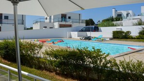 A swimming pool area with a covered section, lounge chairs, and a modern building in the background. - Modern, air-conditioned family apartment with pool. 10 minute walk to beach (Salir do Porto)