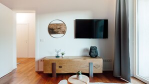 Ein modernes Wohnzimmer mit einem Holzkonsolentisch, einem flachbildfernseher an der Wand und einem großen Fenster mit Vorhängen.
