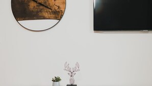 Ein modernes Wohnzimmer mit einem Holzkonsolentisch, einem runden Wandbild, einem an der Wand befestigten Fernseher und einer Weinflasche im Vordergrund.
