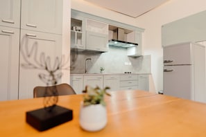 A modern kitchen with white cabinetry, a wooden dining table, and a small potted plant.