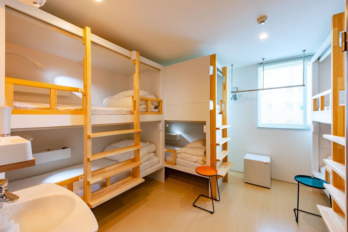 A compact hotel room with bunk beds, a small table, a sink, and a compact refrigerator.
