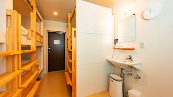 Una habitación de hotel con una cama litera de madera, un lavamanos blanco, un espejo y un reloj en la pared.