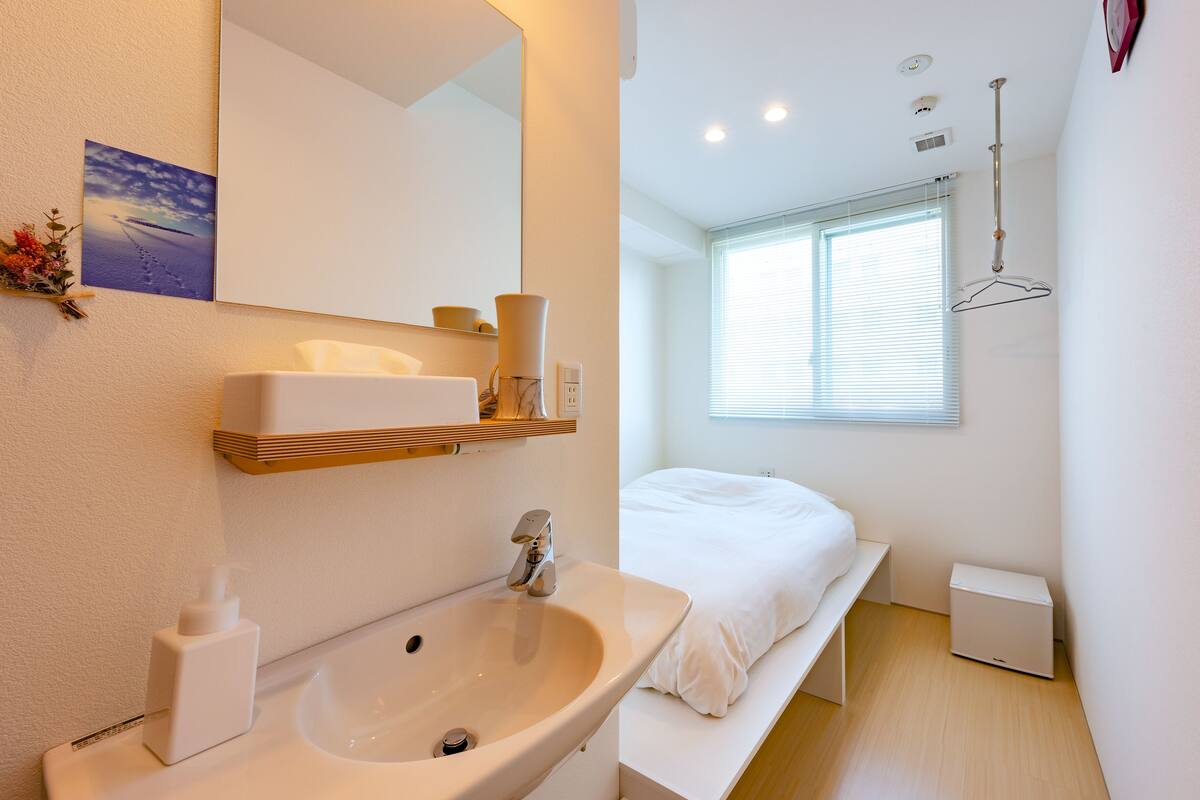 A modern bathroom with a sink, mirror, and a bedside table.