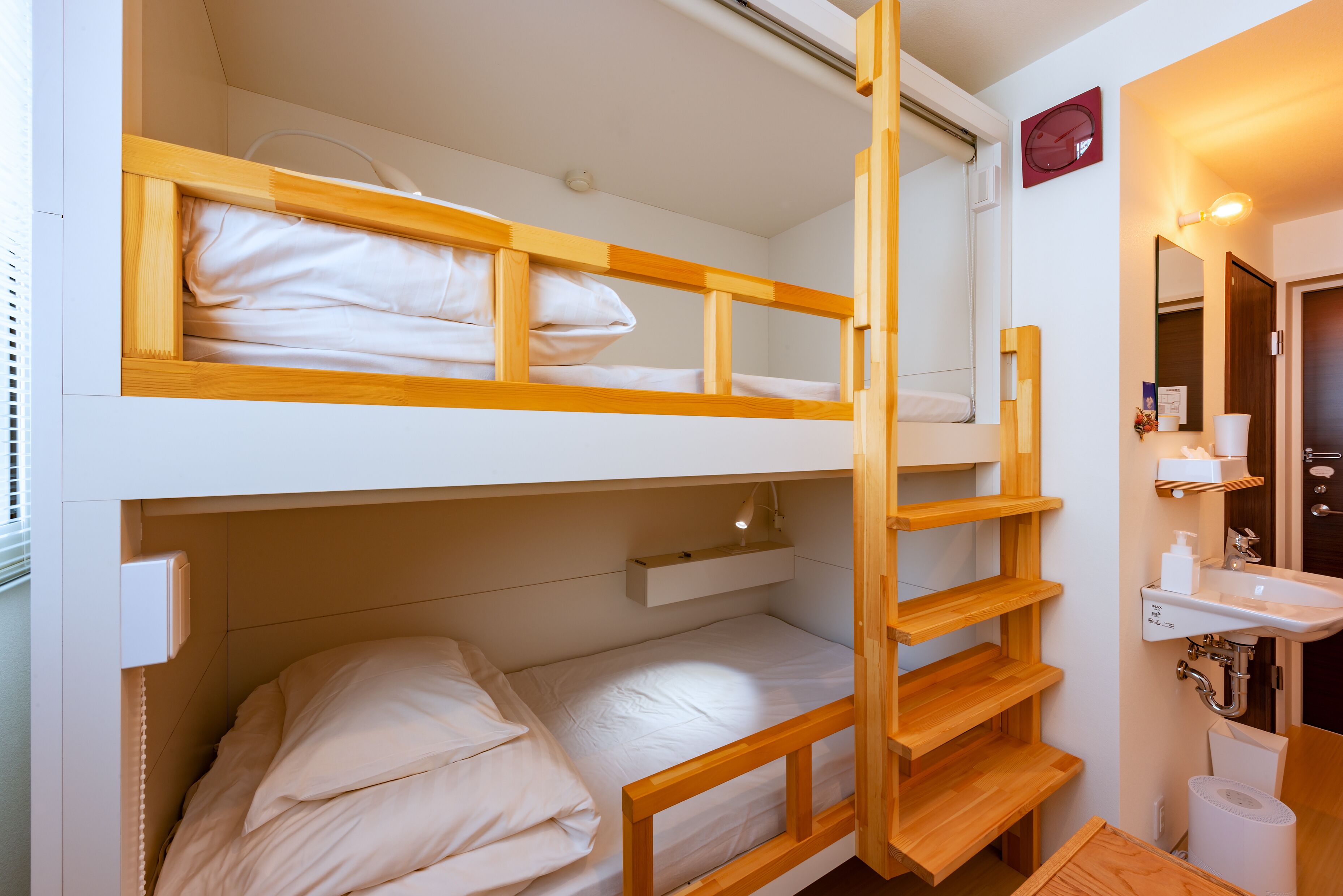 Een slaapkamer met een stapelbed, een houten ladder, een nachtkastje en een klein plankje.