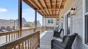 Ein überdachter Balkon mit Holzbalkonen, Korbstühlen und Blick auf umliegende Häuser.