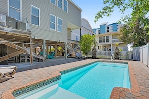 A residential backyard with a swimming pool, a covered patio, and a staircase leading to a second level.