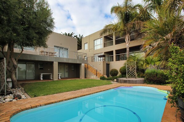 A modern building with a swimming pool, surrounded by greenery and palm trees.