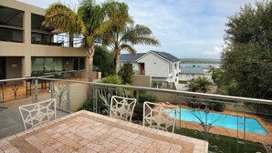 A balcony with a view of a swimming pool, palm trees, and a building with a balcony. - Casa de Palmera, Langebaan 6-sleeper (Langebaan)