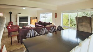 A modern living room with a dark wooden dining table, red leather sofas, and a large window providing a view of greenery. - Casa de Palmera, Langebaan 6-sleeper (Langebaan)