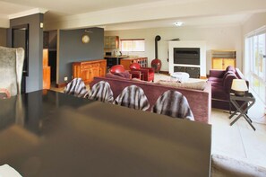 A modern living room with a dark wooden dining table, red and purple sofas, and a kitchen in the background.