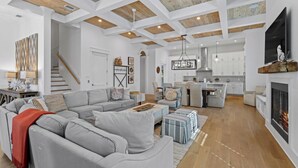 A spacious living room with a grey sectional sofa, a fireplace, and a kitchen in the background.
