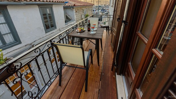 A balcony with a wooden table, two chairs, and a bottle of wine. - Guarda Il Porto Apartment - Hydra port (Idra)