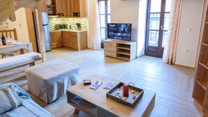 A spacious living area with a wooden floor, a television, a kitchen with wooden cabinets, and a balcony with a view. - Guarda Il Porto Apartment - Hydra port (Idra)