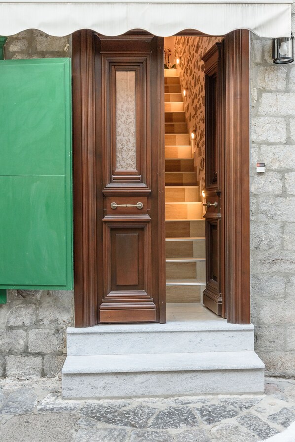 Une porte d’entrée en bois, précédée d’un petit escalier en pierre menant à un escalier.