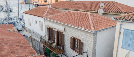 A coastal town with terracotta-tiled buildings, a balcony with outdoor furniture, and a view of boats in the water.
