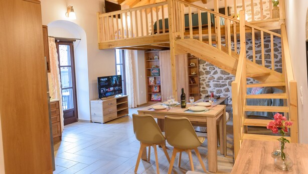 Una habitación acogedora con una escalera de madera, una mesa de comedor con sillas, un televisor y una estantería.