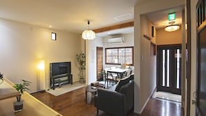A living room with a TV, sofa, dining table, and chairs.