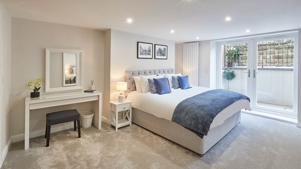 A bedroom with a large bed, a desk, a chair, a lamp, and a window with a view. - The Garden Apartment (Harrogate)
