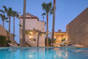 Una piscina con sillas de descanso, palmeras y un edificio con techo de tejas.