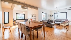 Un vaste espace de vie comprenant une table à manger en bois, un canapé et un fauteuil. On y trouve également une bibliothèque et une fenêtre donnant sur un paysage agréable.