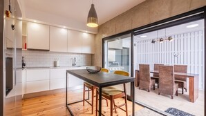 Une cuisine moderne avec des meubles blancs, une table à manger en bois et une porte en verre donnant sur un coin repas équipé de chaises en osier.