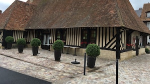 A traditional half-timbered building with a steeply pitched roof, stone foundations, and a cobblestone courtyard. - Cabourg Mon Amour (Cabourg)