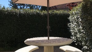 A round table with a tiled top and two white benches, surrounded by gravel. - Cabourg Mon Amour (Cabourg)