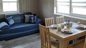 A dining area with a wooden table set for four, surrounded by wooden chairs. There is a blue sofa with decorative pillows in the background. - Sunny Paradise-s?oneczny Raj (Sarbinowo)