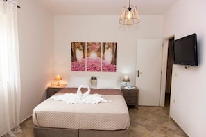 Une chambre d’hôtel avec un lit, un tableau représentant un chemin rose, une télévision et une porte.