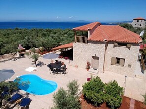 Una villa de piedra con piscina, mobiliario exterior y vistas al mar.