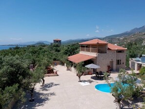 A villa with a pool, outdoor seating, and a view of the sea and mountains.