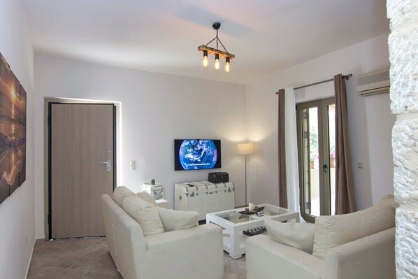 Una sala de estar moderna con un conjunto de sofás, una mesa de centro, un televisor montado en la pared y una lámpara del techo.