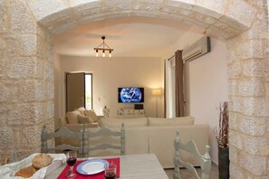 Un rincón acogedor con un arco de piedra, televisor, sofá y una mesa de comedor dispuesta con pan y vino.