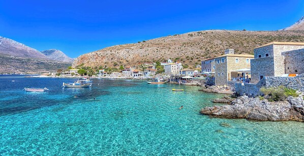 Ein Küstendorf mit klarem türkisblauem Wasser, Booten und Steinhäusern.