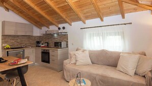 A compact kitchen with modern appliances, a dining area with a table and chairs, and a living area with a sofa. - Selinitsa Stone Studio - Mani Seaview Retreat (Agios Nikolaos)