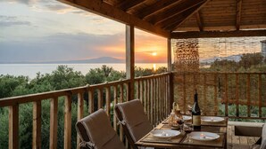 A wooden deck with a table set for dining, overlooking a body of water and a sunset. - Selinitsa Stone Studio - Mani Seaview Retreat (Agios Nikolaos)